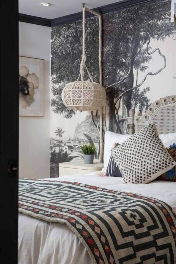 A bedroom with a patterned bedspread, a hanging light fixture, and a mural on the wall.