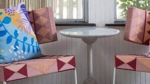 A sunroom with two cushioned seating areas facing a large window, a small round table, and a decorative ceramic piece.