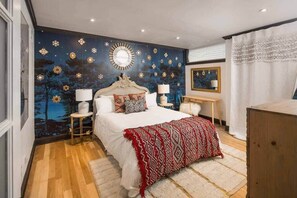 A bedroom with a bed, bedside tables, a mirror, and a dresser.