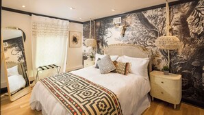 A bedroom with a large bed, a nightstand, a dresser, a mirror, and a wall mural.