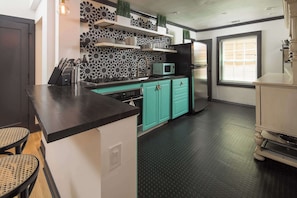 Une cuisine avec des armoires de couleur turquoise, un plan de travail noir, un four à micro-ondes et un réfrigérateur.