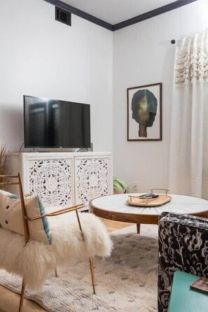 Un salon moderne doté d’un téléviseur à écran plat, d’une table basse ronde et d’un meuble blanc orné de motifs sculptés complexes.