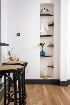 A room with a white wall, a built-in shelf with decorative items, and a wooden floor. - Bohemian Rhap (Atlanta)