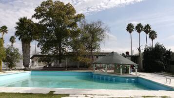 Relax by the serene pool surrounded by lush greenery and palm trees, under the shaded gazebo.