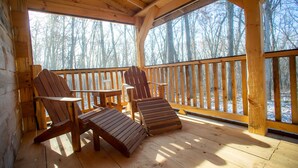 A wooden deck with two Adirondack chairs and a table, overlooking a forest. - Tanager cabin at Driftless Creek (Viroqua)