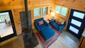 A cabin with a fireplace, two blue sofas, a rug, and a window overlooking a deck. - Tanager cabin at Driftless Creek (Viroqua)