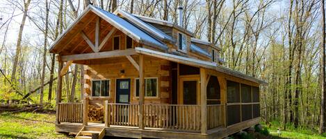 A wooden cabin with a porch, large windows, and a chimney.