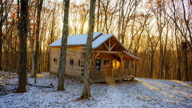 A cabin with a porch and a stone exterior, surrounded by a forest. - Tanager cabin at Driftless Creek (Viroqua)