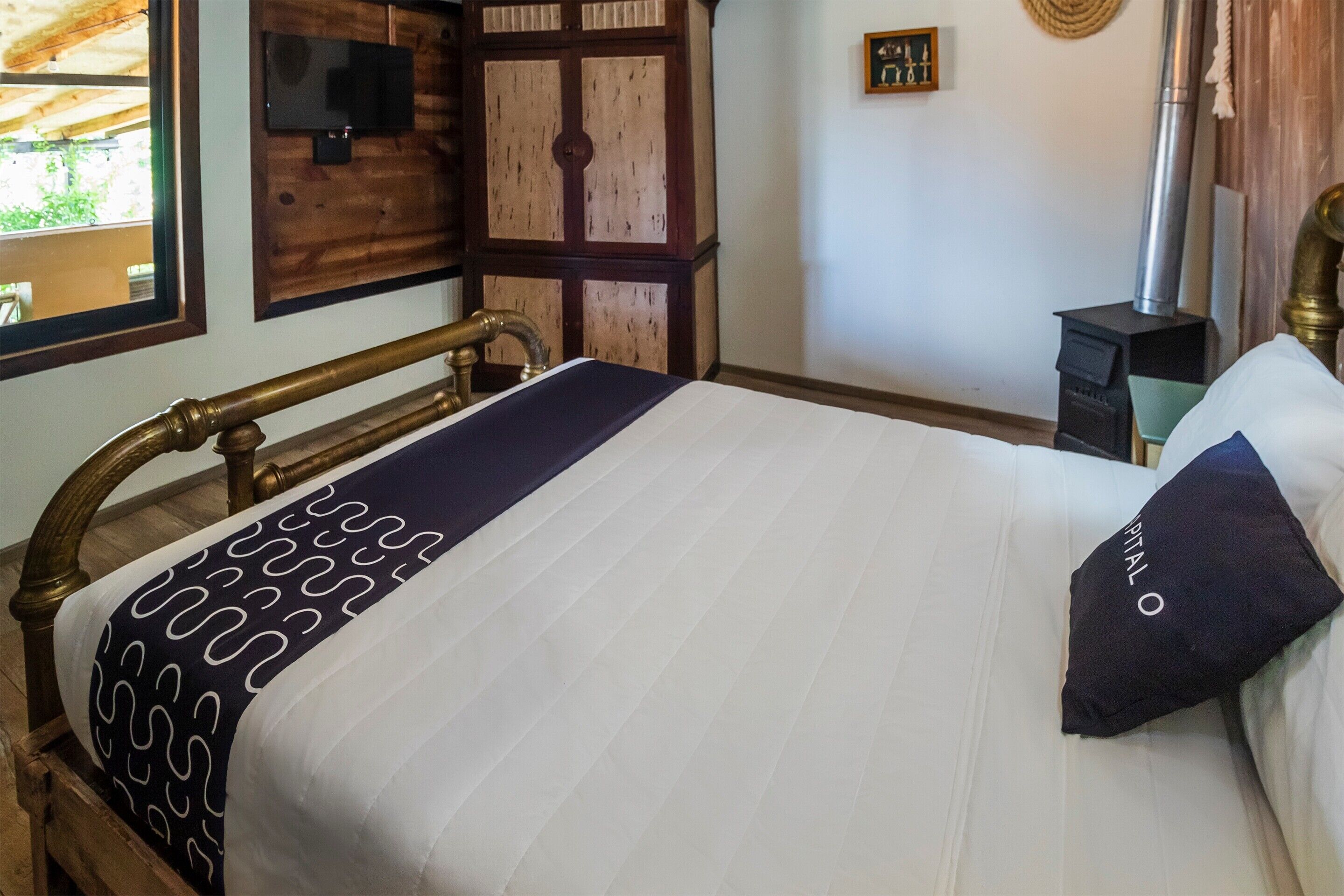 Un dormitorio con estructura de cama de madera, colchón blanco, manta con estampado y almohada oscura con la palabra 'ITALY'.