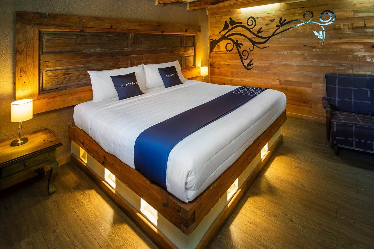 A wooden-framed bed with white bedding and a blue accent, a nightstand with a lamp, and a wooden wall with a decorative design.