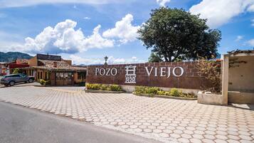 Un muro de ladrillo con el letrero "POZO VIEJO" y un área de acceso pavimentada.
