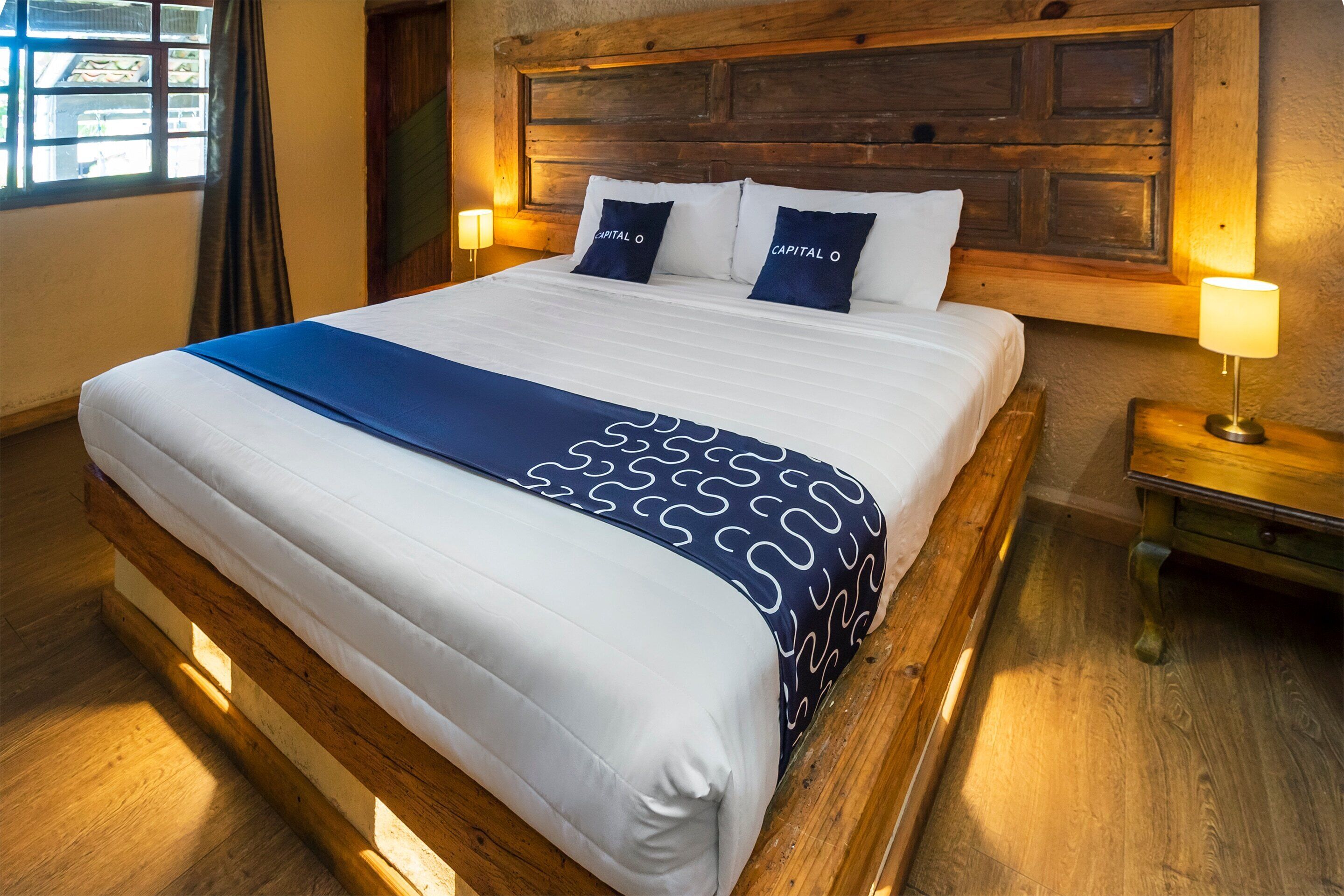 Una cama bien tendida con ropa de cama blanca y azul marino, un cabecero de madera y dos lámparas de noche.