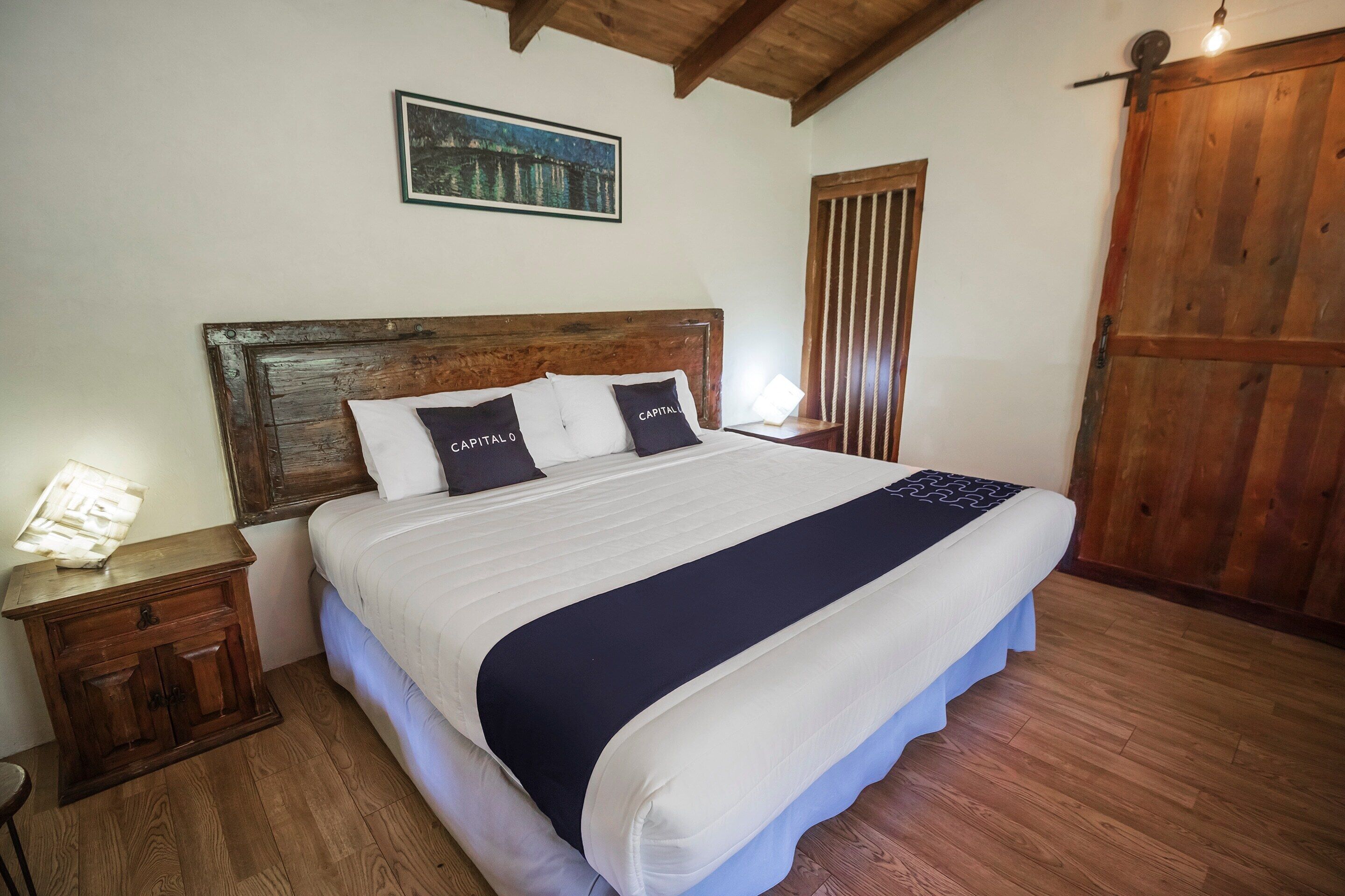 A neatly made bed with a wooden headboard, a nightstand with a lamp, and a wooden floor.