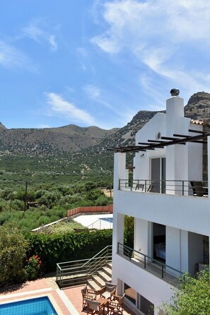 A modern two-story building with a balcony, a pool, and a view of a mountainous landscape.