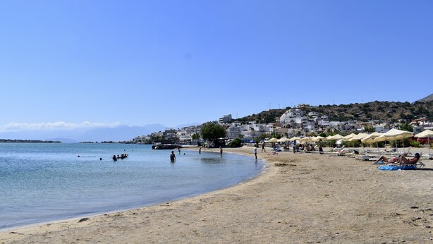 A beach with clear blue water, people swimming, and beach umbrellas.
