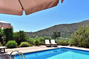 Une piscine entourée de chaises longues et de parasols, bordée de verdure et avec une chaîne de montagnes en toile de fond.