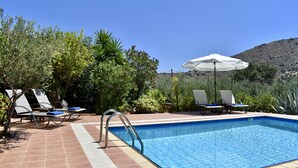 A swimming pool with lounge chairs and umbrellas, surrounded by greenery and a hilly landscape.