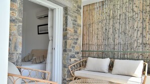 A room with a stone wall, a woven sofa, a wicker chair, and a glass table.