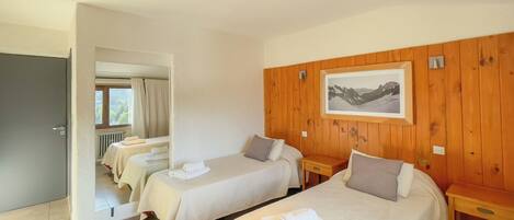 A hotel room with two single beds, a wooden panel wall, a framed picture, and a view through an open door.