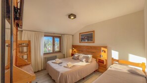 Ein Schlafzimmer mit einem hölzernen Kopfteil, einem großen Bett mit Kissen und Decke, einem Nachttisch mit Lampe, einem Fenster mit Vorhängen und einer Heizung.
