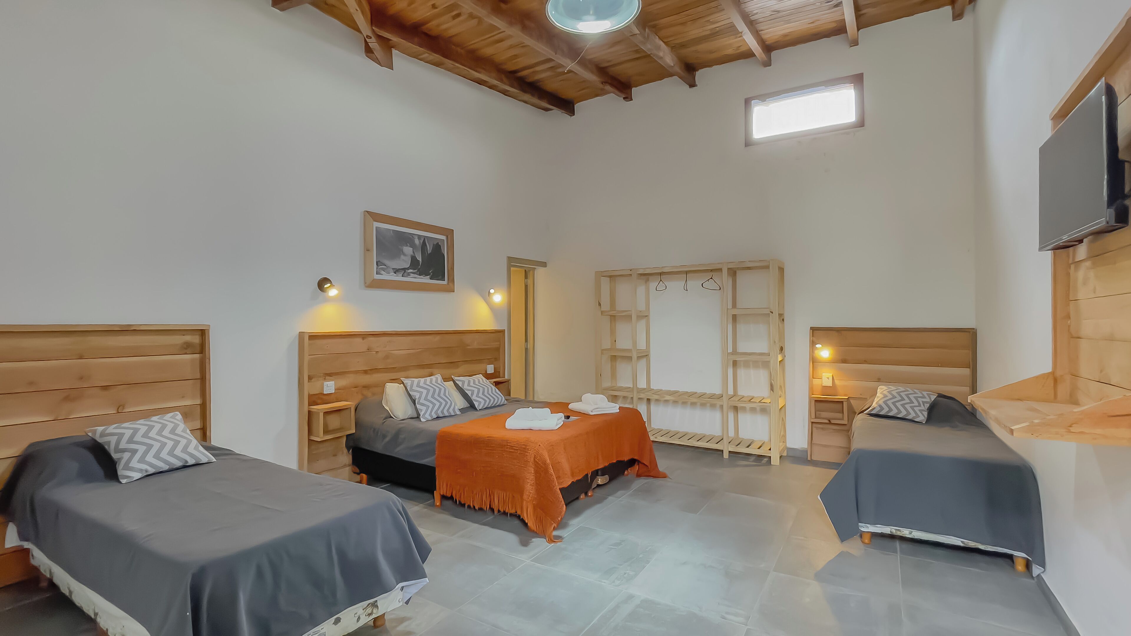 Una habitación con tres camas, cabeceros de madera, un pequeño estante de madera, una escalera y un cuadro enmarcado en la pared.