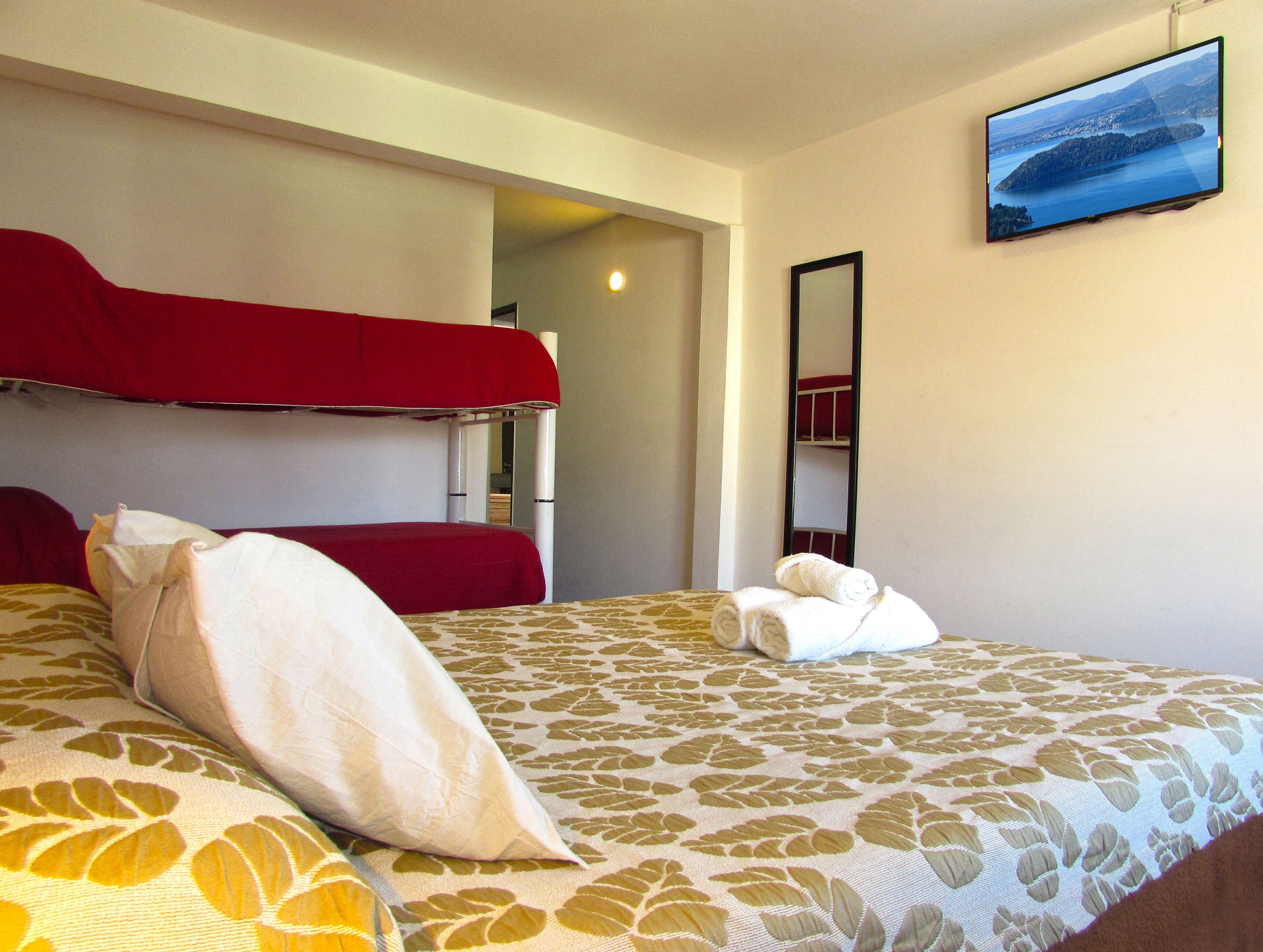 Habitación de hotel con literas, una cama individual, un espejo y un televisor en la pared.