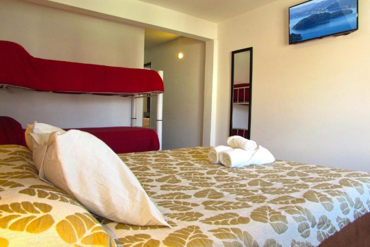 Une chambre d'hôtel avec un lit superposé, un lit recouvert d'une literie à motifs floraux, un téléviseur à écran plat fixé au mur et un miroir.