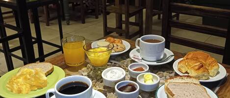 A breakfast table with plates of food, cups, and a glass of orange juice.