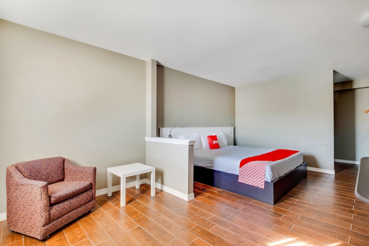 Una habitación de hotel pequeña con una cama, una mesita blanca y un sillón estampado.
