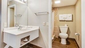 A bathroom with a white sink, mirror, and vanity, a toilet, and a shower area. - OYO Hotel Elk City OK Route 66 (Elk City)