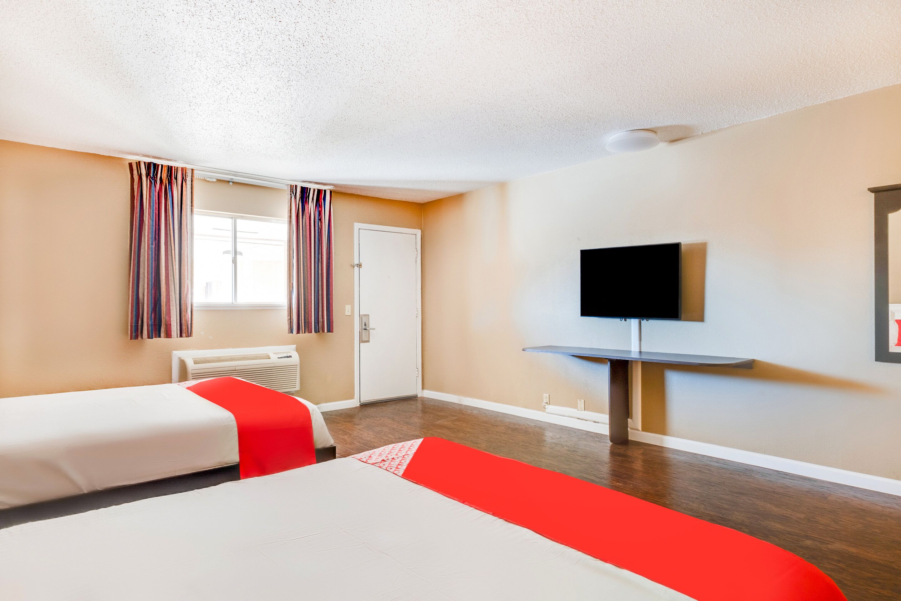 A hotel room with two beds, a television, a window with curtains, and a wall-mounted TV.