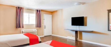 Habitación de hotel con dos camas, una televisión, una ventana con cortinas y una televisión montada en la pared.