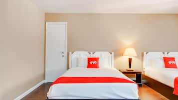 A hotel room with two beds, a door, a nightstand with a lamp, and a red and white bedspread.