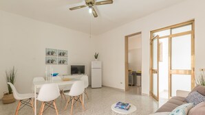 Een moderne woonkamer met een eethoek, een keuken op de achtergrond en een groot raam.
