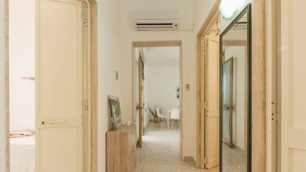 Een gang met een houten kast, een spiegel en een deur naar een andere kamer.