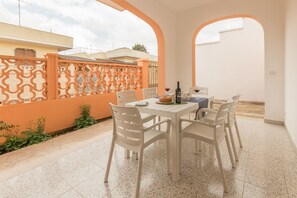 Een terras buiten met een tafel en stoelen, een decoratieve hek en een uitzicht op naburige gebouwen.