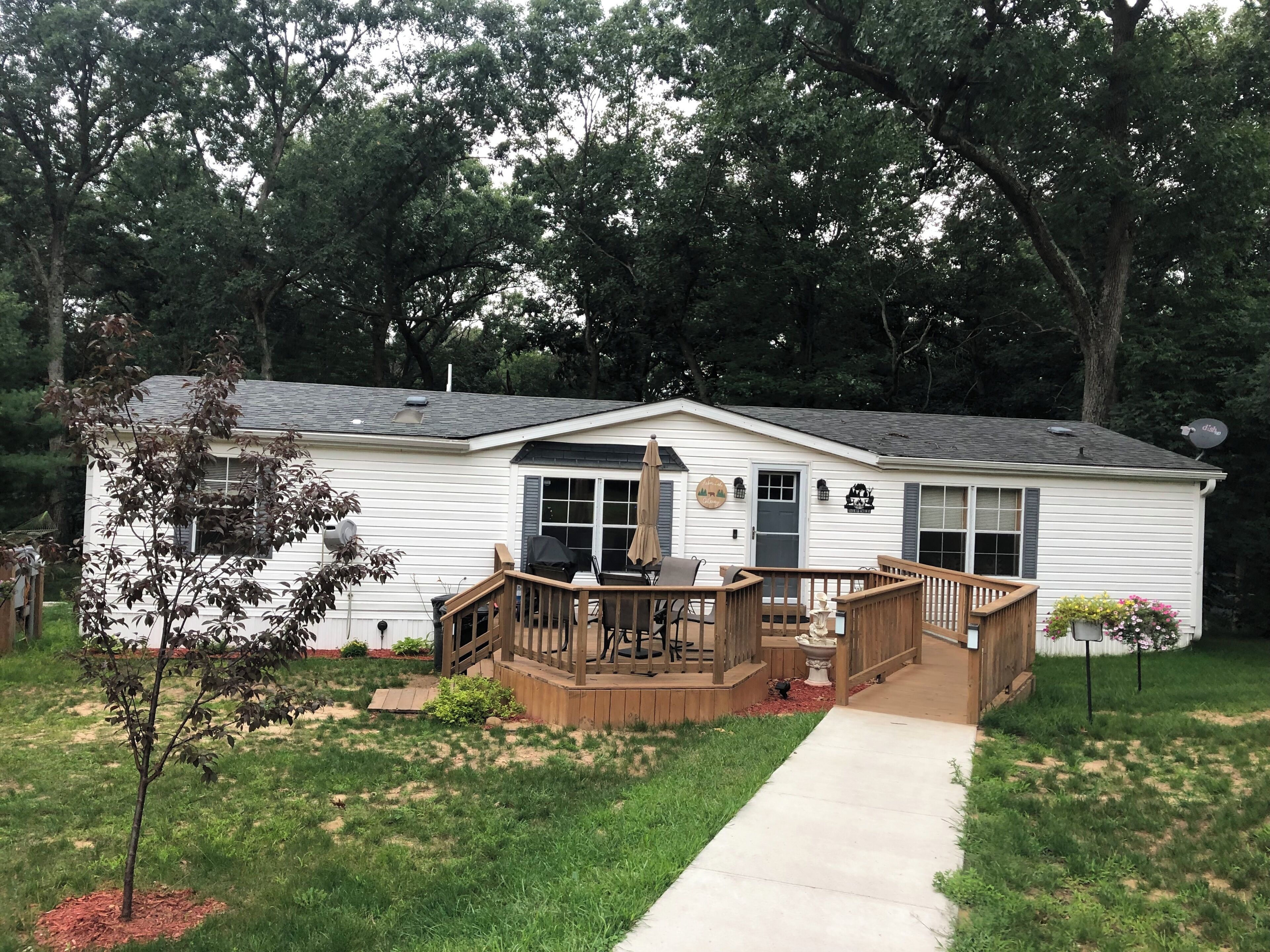 A single-story house with a front deck, a satellite dish, and a small garden area.
