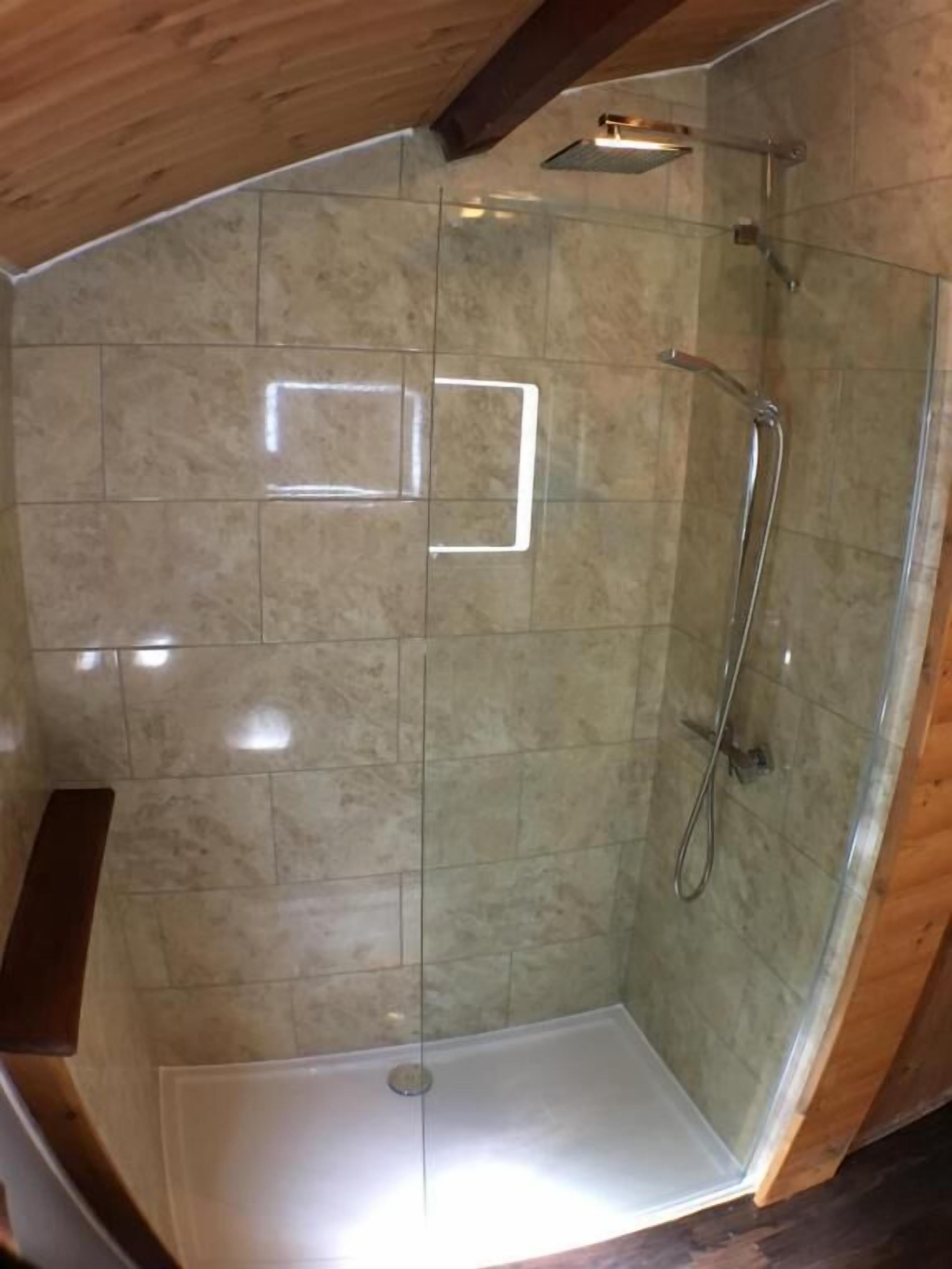 A glass-enclosed shower area with a tiled floor and a wooden ceiling.