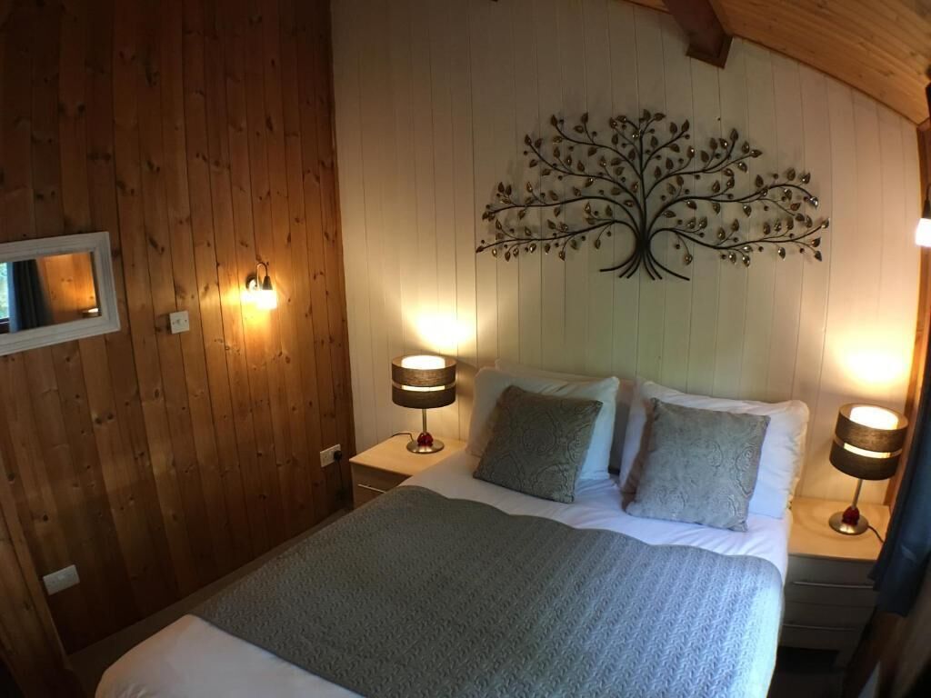 A cozy bedroom with a wooden ceiling, a bed with a grey blanket, two bedside lamps, and a wall-mounted tree decoration.