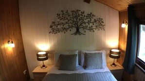 A bedroom with a bed, two bedside lamps, a wall-mounted tree decoration, and wooden paneling. - Snowdrop 14 Hot Tub (Carmarthen)