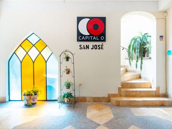 A hotel entrance with a stained glass door, a wall-mounted sign reading "CAPITAL O SAN JOSE", and a staircase leading to an upper floor.