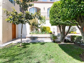 A courtyard with a well-maintained lawn, a stone bench, and various potted plants.