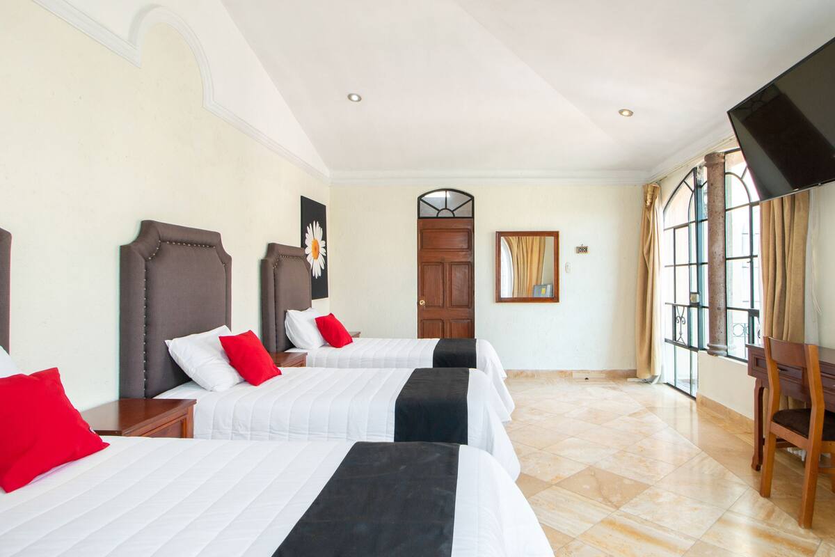 Habitación de hotel con dos camas, una puerta de madera, un ventanal grande y un espejo.