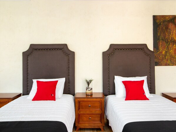 Two twin beds with brown headboards, white bedding, and red pillows.