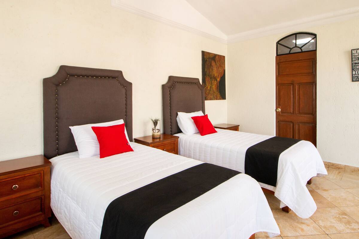 Dos camas con cabeceras, ropa de cama blanca y almohadas rojas.