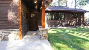 Una cabaña de madera con base de piedra, una puerta principal y una ventana con vista a un patio cubierto de césped.