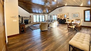 Amplia sala de estar con techo alto y suelo de madera, que cuenta con chimenea, asientos y zona de comedor.