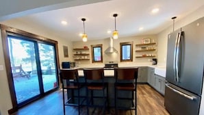 Una cocina moderna con una isla central, taburetes de bar, un refrigerador y un amplio ventanal con vistas al exterior.