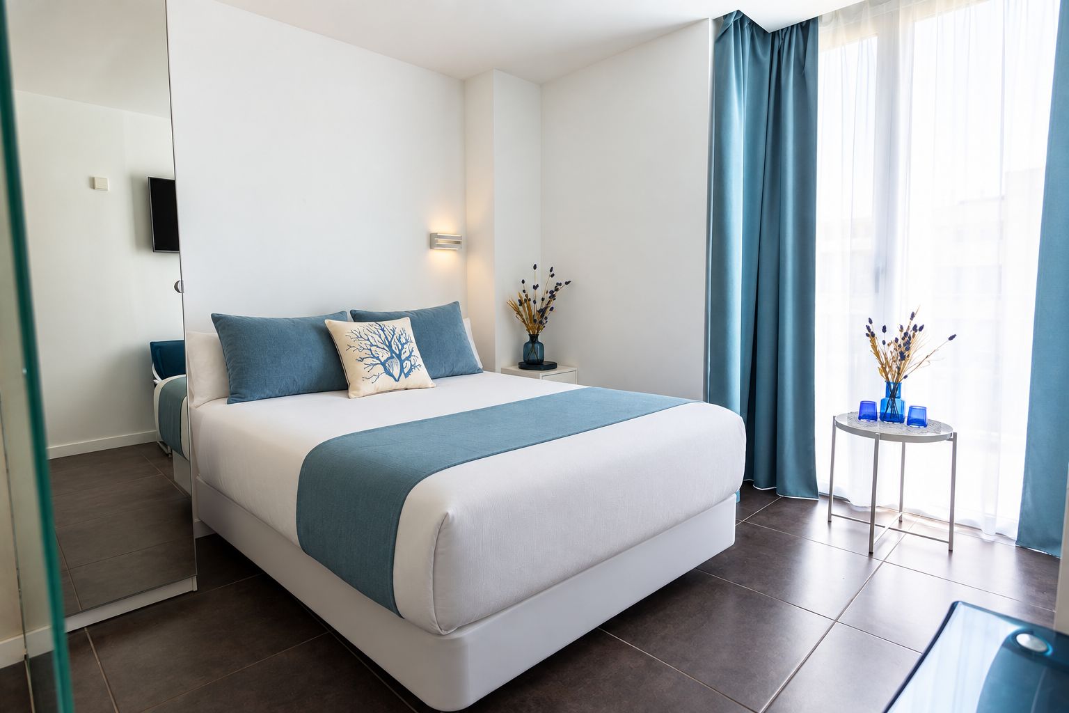 Ett modernt hotellrum med en stor säng, ett nattduksbord med en vas och utsikt över omgivningarna genom ett fönster med blå gardiner.
