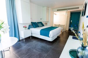 A modern hotel room with a bed, bedside table, and a small desk with a chair.